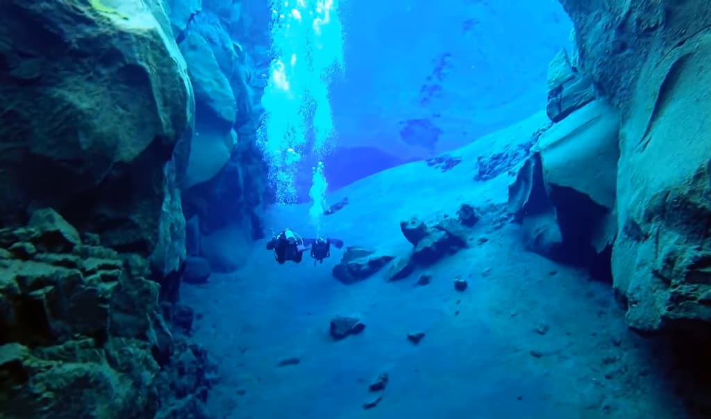 Des plongeurs explorent un canyon sous-marin, rayons de lumière perçant l'eau