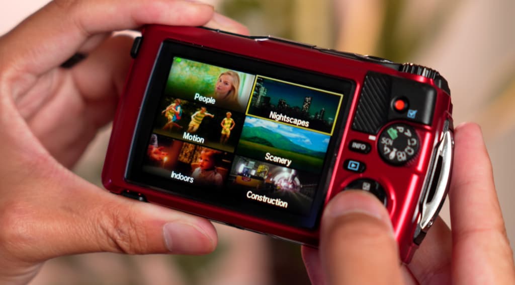 Des mains tenant un appareil photo rouge avec un écran affichant des menus