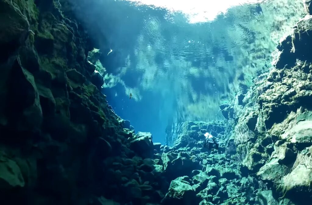 Plongeurs explorent fissure sous-marine, éclairée par soleil, grouillant d'affleurements rocheux