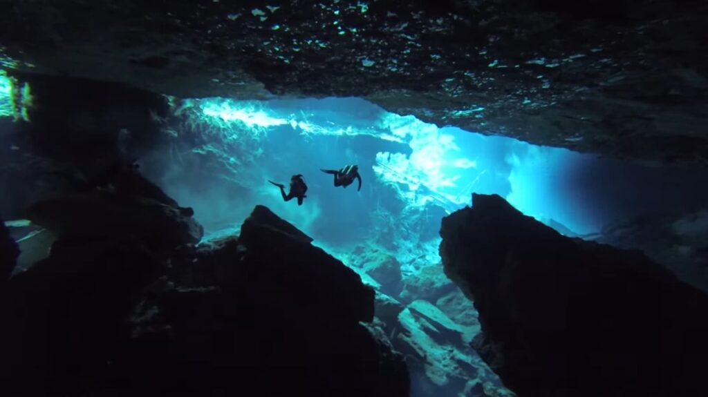 Deux plongeurs sous des rayons de lumière dans une caverne aquatique